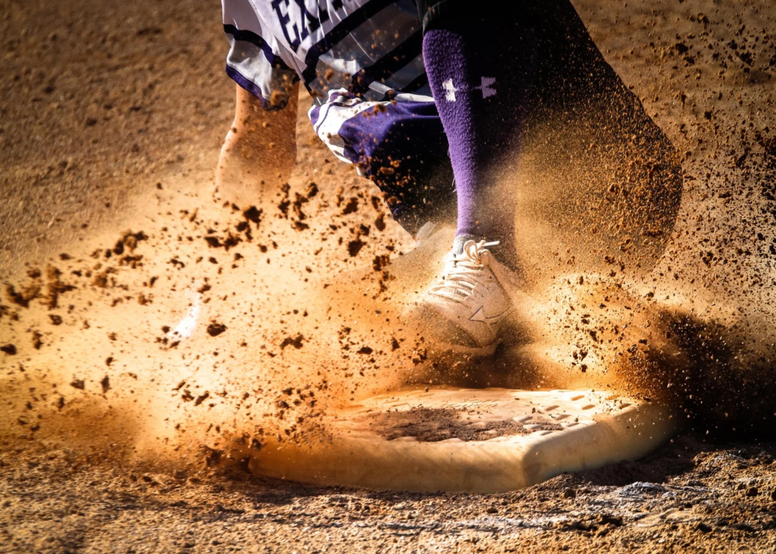Softball player sliding into base with dust cloud